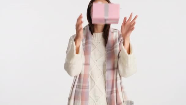 Attractive cheerful girl with cozy plaid on shoulders happily throws up gift box over white background - Metraje, vídeo