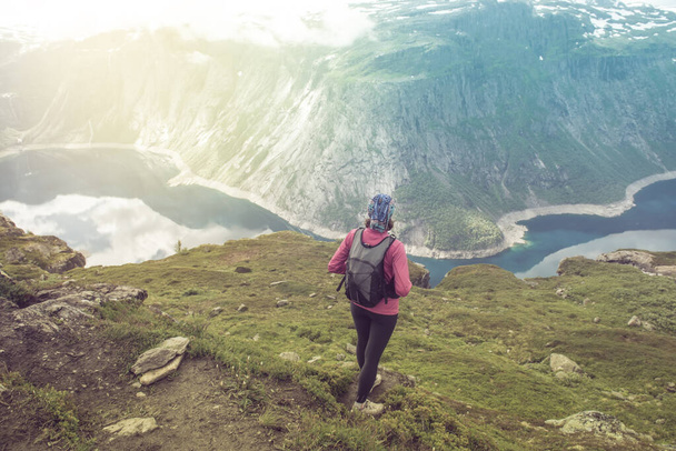 Young woman with backpack standing on fjord coast - Foto, imagen