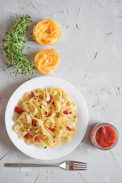 Macarrão tradicional italiano tagliatelle com tomates secos e tomilho em um fundo leve espaço de cópia vista superior
 - Foto, Imagem