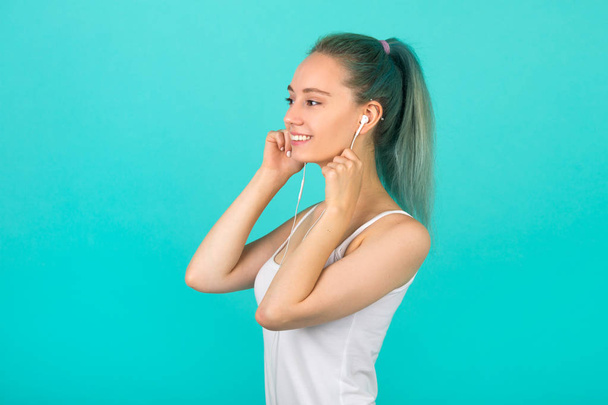 beautiful young slim woman in sportswear on a blue background listens to music - Photo, image