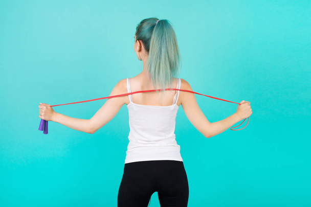 beautiful young slim woman in sportswear on a blue background with a skipping rope in hands - Fotoğraf, Görsel