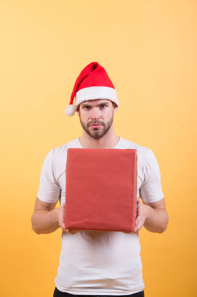 Delivery service. Courier occupation. Wish list. Man handsome wear santa hat hold gift box. Hipster hold christmas gift. Give gift spread happiness. Congratulations concept. Christmas greetings - Photo, image