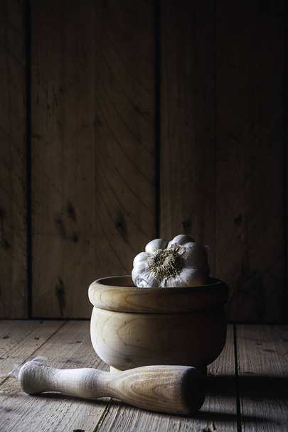 Biały czosnek z zaprawą drewnianą na drewnianym stole i ciemnym tle. Rustykalna fotografia żywności - Zdjęcie, obraz