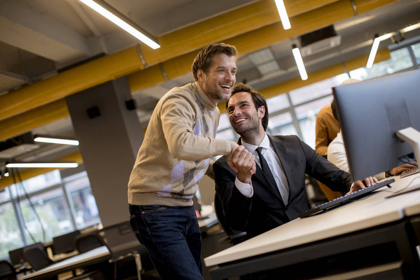 Happy young businessmen handshaking by the table in the modern office - Foto, imagen