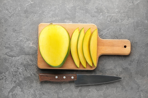Board with cut mango fruit and knife on grunge background - 写真・画像