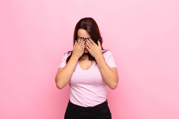 young pretty woman feeling sad, frustrated, nervous and depressed, covering face with both hands, crying against pink wall - Foto, imagen