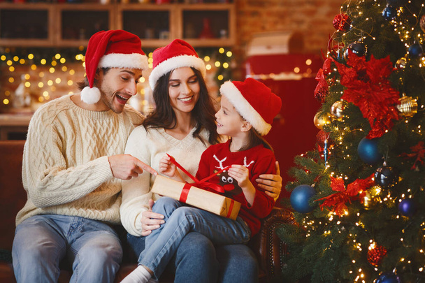 Little świąteczny dziewczyna otwarte prezenty Boże Narodzenie z mamą i tatą - Zdjęcie, obraz