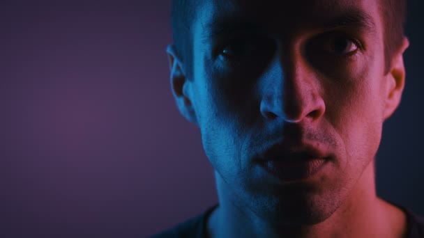 Portret van een man die je neukt in neonlicht. Agressief afgestelde man toont middelvinger in een donkere kamer verlicht door neon licht. - Video