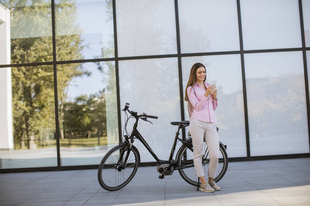 Досить молода жінка використовує мобільний телефон сучасним міським електричним електронним велосипедом як чистий стійкий міський транспорт
 - Фото, зображення