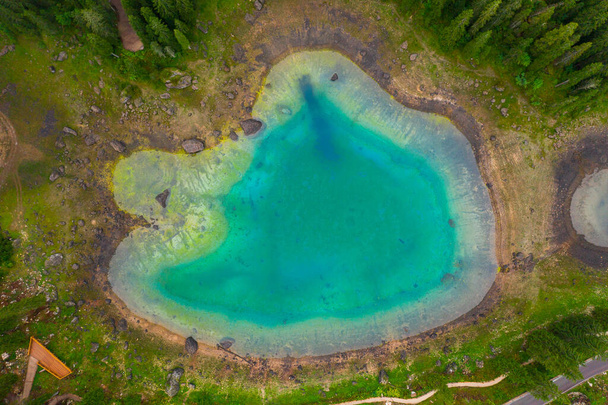 Αεροφωτογραφία του γαλαζοπράσινα νερά της λίμνης Carezza στις Άλπεις Δολομίτες. Lago di Karersee κοντά στο δάσος ελάτης. - Φωτογραφία, εικόνα