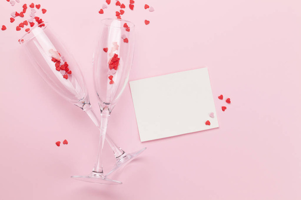 Champagnergläser und herzförmige Süßigkeiten Urlaubsvorlage. Weihnachten, Geburtstag oder Valentinstag vor rosa Hintergrund. Ansicht von oben mit Platz für Ihre Grüße. flache Lage - Foto, Bild