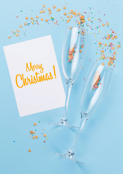 Copas de champán, tarjeta de felicitación de Navidad y dulces sobre fondo azul. Vista superior. Puesta plana
 - Foto, imagen