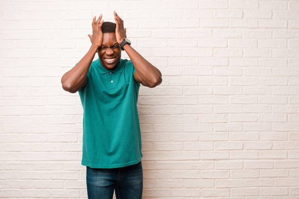 giovane afroamericano nero sentirsi stressato e ansioso, depresso e frustrato con un mal di testa, alzando entrambe le mani a testa contro muro di mattoni
 - Foto, immagini