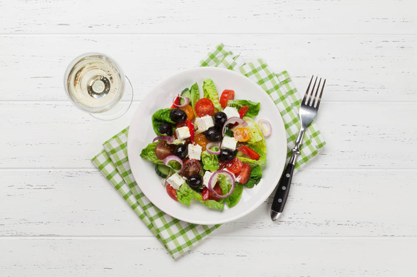 Salada grega com pepino, tomate, pimenta, alface, cebola, queijo feta e azeitonas, vestida com azeite. Vista superior com copo de vinho branco
 - Foto, Imagem