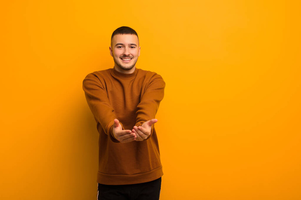young handsome man smiling happily with friendly, confident, positive look, offering and showing an object or concept against flat background - Fotografie, Obrázek