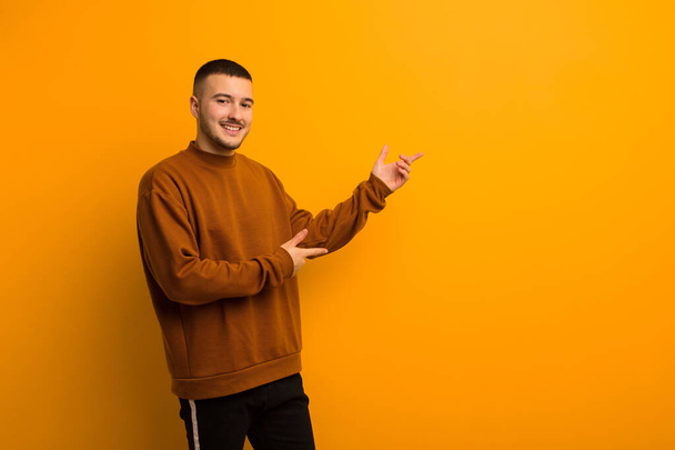 young handsome man smiling proudly and confidently, feeling happy and satisfied and showing a concept on copy space against flat background - Fotografie, Obrázek