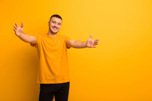 young handsome man smiling cheerfully giving a warm, friendly, loving welcome hug, feeling happy and adorable against flat background - Фото, изображение