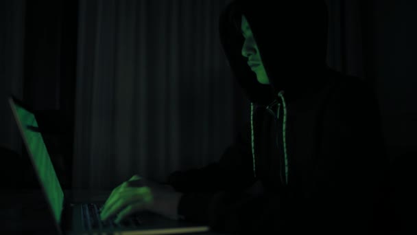 Hacker, die in das Computernetzwerk eindringen. Ein junger Mann in einem dunklen Raum tippt auf einem Laptop. Hacker mit Laptop. e-der Räuber. einsamer Teenager im Online-Chat. Computerkriminelle. 4k Filmmaterial. - Filmmaterial, Video