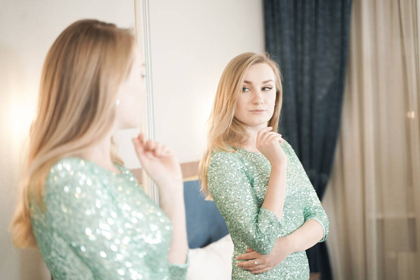 bonita mujer joven en apretado vestido de noche de brillo corto listo para la fiesta y mirando el espejo en ti mismo
 - Foto, Imagen