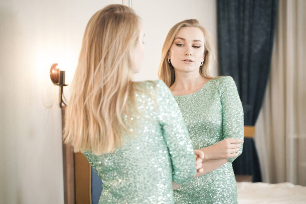 ładna młoda kobieta w krótkim brokatu sukienka wieczorowa gotowa do partii i patrząc w lustro na siebie - Zdjęcie, obraz