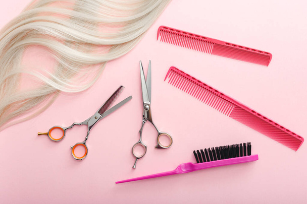 Scissors, combs and other hairdresser's accessories and strand of blonde hair on pink background. Flat lay with space for text. Hairdresser service. Beauty salon service - Zdjęcie, obraz
