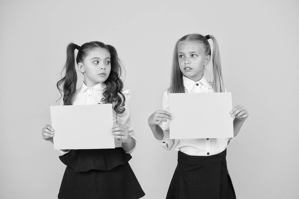 Thinking over a home work. Little children holding empty sheets for examination work on yellow background. Small girls with blank green papers for project work or research. Paper work, copy space - Foto, Imagen