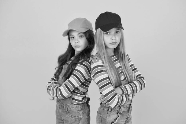 Fashion that matches their conscious style. Small girls in style keeping arms crossed on yellow background. Little children wearing baseball caps in casual streetwear style. Hip hop or hipster style - Foto, Bild