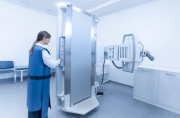 Blurred photo of woman in special protective costume preparing X-ray equipment - Photo, Image