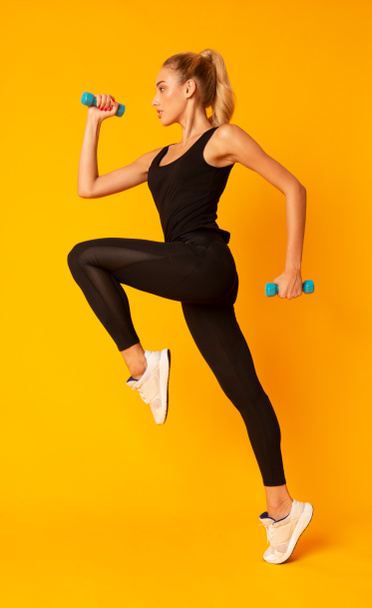 Fitness lány ugrás gazdaság Dumbbells több mint sárga háttér, Studio Shot - Fotó, kép