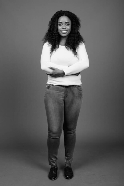 Studio shot της νεαρής όμορφης Αφρικανικής γυναίκας με μαλλιά Afro σε γκρι φόντο σε μαύρο και άσπρο - Φωτογραφία, εικόνα