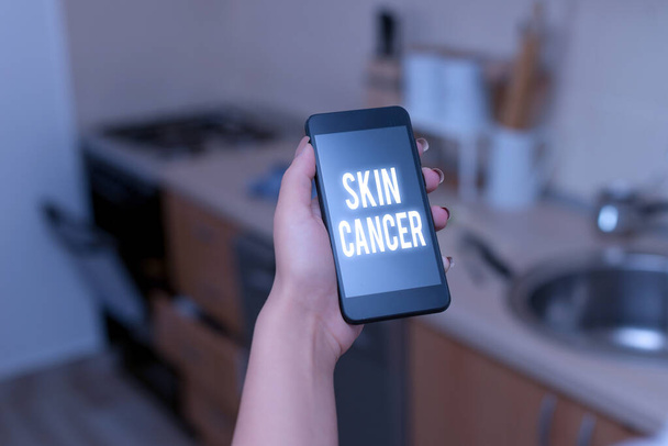 Εννοιολογική γραφή χεριών που δείχνει καρκίνο του δέρματος. Επαγγελματική φωτογραφία κείμενο ανεξέλεγκτη ανάπτυξη των ανώμαλων κυττάρων του δέρματος λόγω της έκθεσης στον ήλιο γυναίκα χρησιμοποιώντας smartphone και τεχνολογικές συσκευές μέσα στο σπίτι. - Φωτογραφία, εικόνα