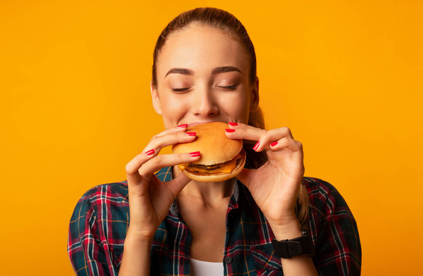 Hambrienta joven mordiendo hamburguesa de pie, Studio Shot
 - Foto, imagen