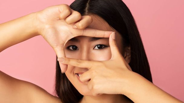 Mulher asiática olhando através de quadro com dedos
 - Foto, Imagem