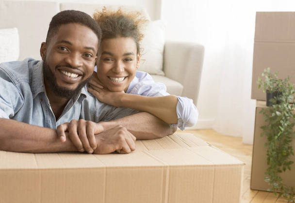 Afro coppia abbracciare seduta tra scatole in movimento in nuovo appartamento
 - Foto, immagini