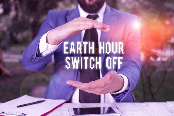 Escrita de mão conceitual mostrando Earth Hour Switch Off. Foto de negócios mostrando The Lights Out Evento Anual Movimento Planeta Dia Homem na frente da mesa. Telemóvel e notas na mesa
. - Foto, Imagem
