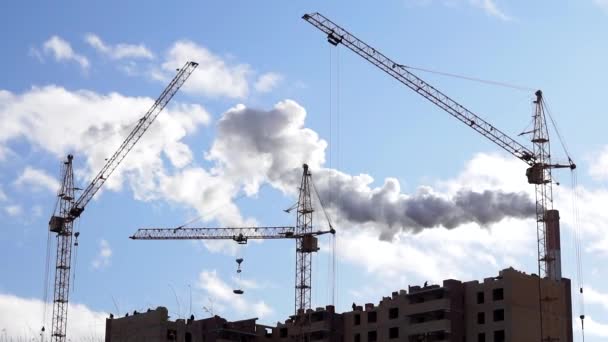 Woningbouw, bouwkranen op de achtergrond van de fabriek, de rook uit de schoorstenen, bouw, milieuvervuiling - Video