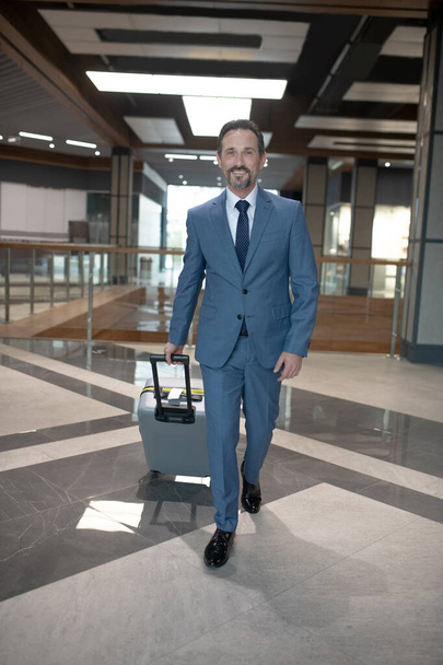 Elegant businessman wearing stylish suit walking with luggage in hotel - Photo, image