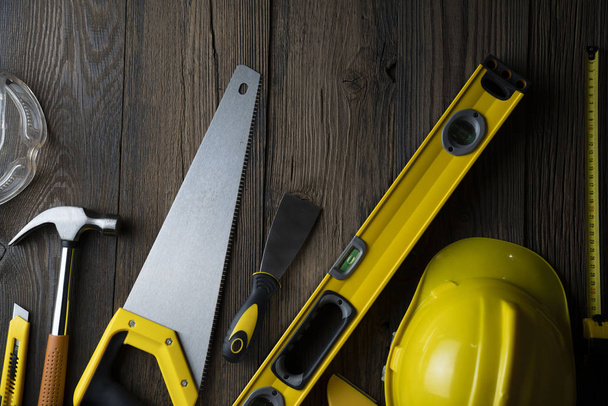 Contractor concept. Yellow hardhat, libella and other tools on the rustic wooden background. - Photo, Image