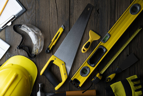 Contractor concept. Yellow hardhat, libella and other tools on the rustic wooden background. - Photo, Image