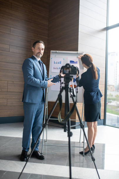 Businessman standing near camera while filming blog with businesswoman - Фото, изображение