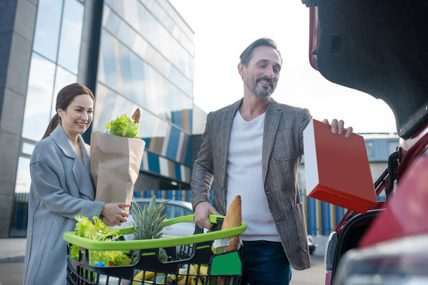 Smiling couple putting their foods into car after groceries shopping - Photo, Image