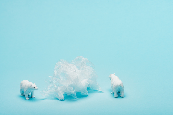 Toy polar bears with plastic packet on blue background, animal welfare concept - Fotó, kép