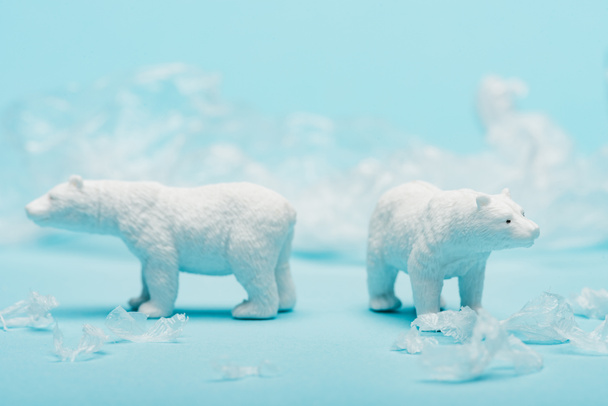 Two toy polar bears with polyethylene trash on blue background, animal welfare concept - Photo, Image