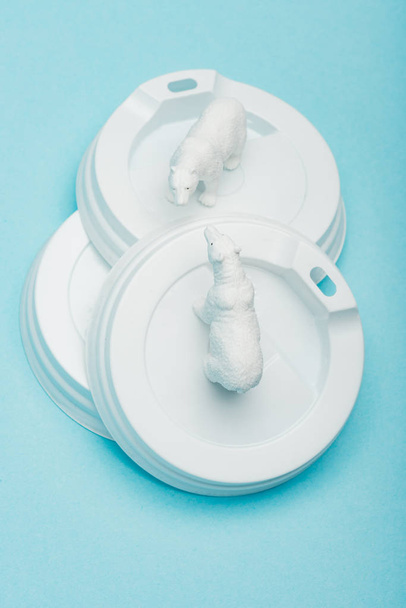 Top view of toy polar bears on plastic coffee lids on blue background, ecological problem concept - Photo, Image