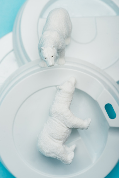 Top view of toy polar bears on plastic coffee lids on blue background, animal welfare concept - Photo, Image