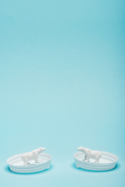 Two toy polar bears on coffee lids on blue background with copy space, animal welfare concept - Photo, Image