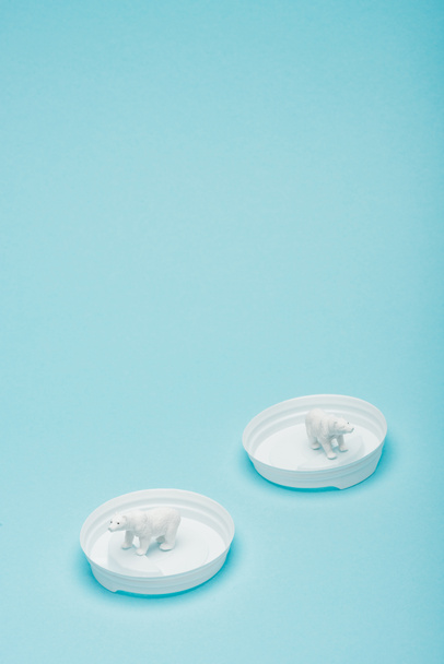 White toy polar bears on plastic coffee lids on blue background, animal welfare concept - Photo, Image