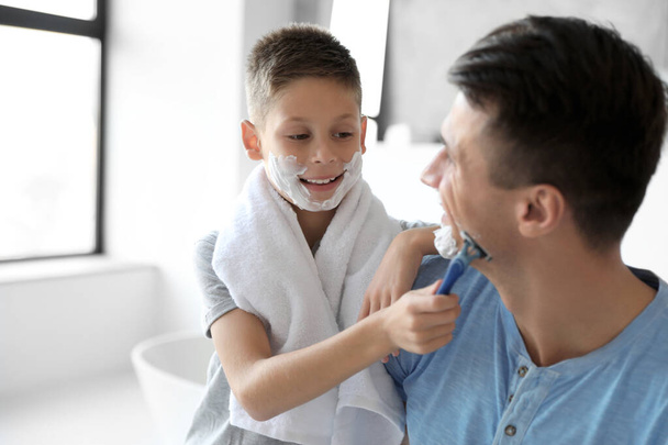 Son shaving his father with razor in bathroom - Foto, immagini