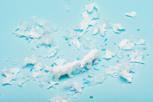 Toy polar bears with polyethylene and plastic pieces on blue background, environmental pollution concept - Photo, Image