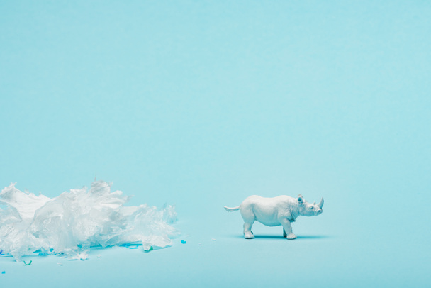 White rhinoceros toy and plastic garbage on blue background, animal welfare concept - Fotoğraf, Görsel